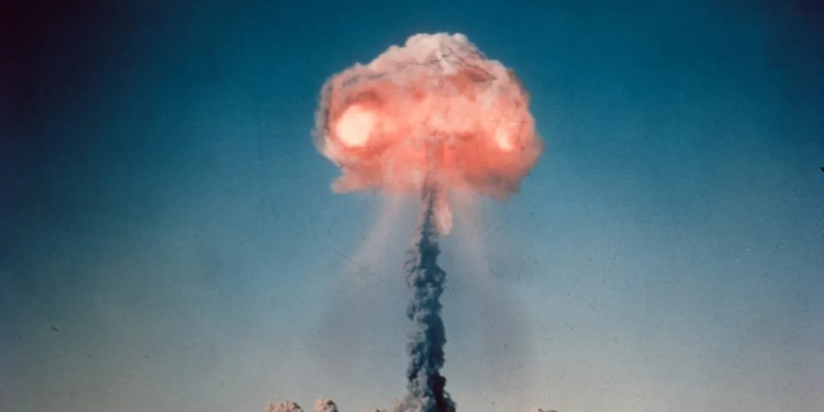 vintage 35mm slide scan of a historic atom bomb explosion and mushroom cloud exploding in the middle of the desert mountain range on the horizon scratches on film dust cloud on the ground and tall mushroom cloud glowing and raining down