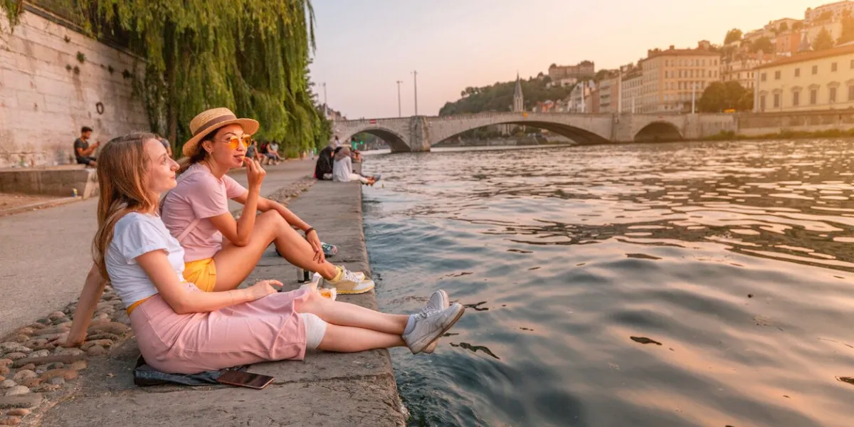 two happy caucasian and asian girls friends meeting great sunset on a river saone in lyon city travel and lifestyle in france