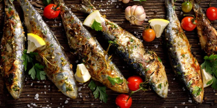 fried fishes with addition of herbs, spices and lemon slices on a wooden background seafood, sardines