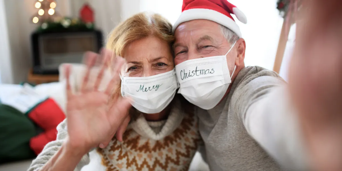 front view of happy senior couple with face masks indoors at home at christmas, taking selfie