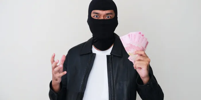 bad guy wearing balaclava holding paper money that he steal