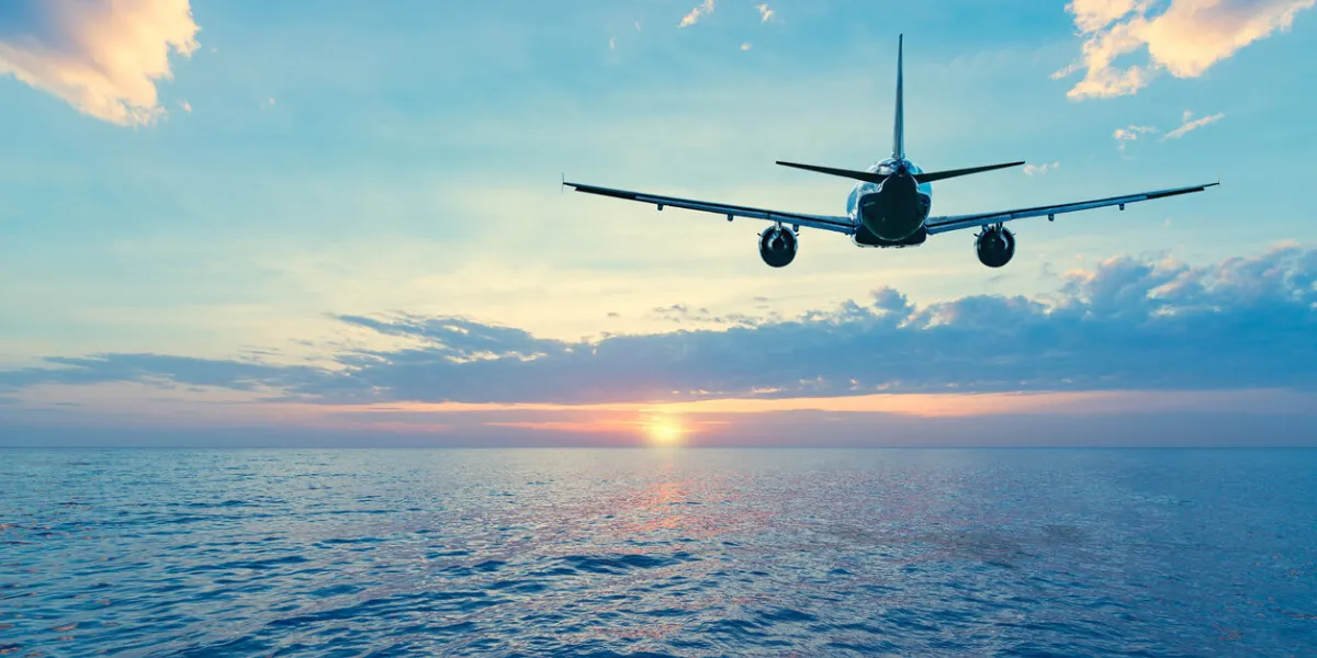 flying of the passenger plane above the sea surface at sunset time