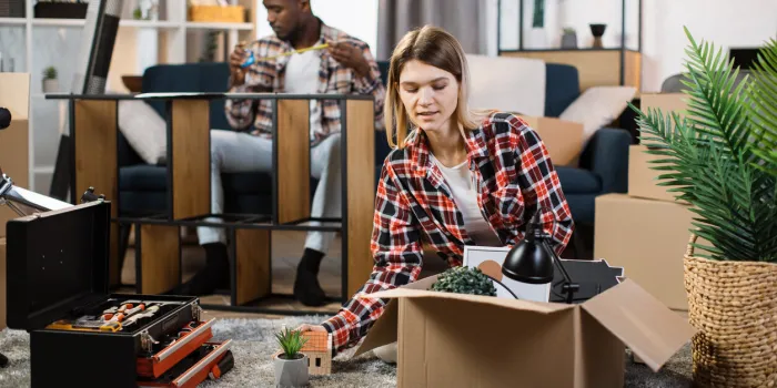 positive caucasian woman unpacking cardboard boxes on floor while focused african american man measuring size of bookcase multicultural couple moving to their new house
