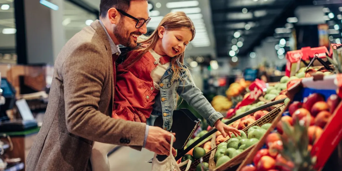 little girl is buying groceries in the supermarket with her father he carrying her and picking together fresh fruits