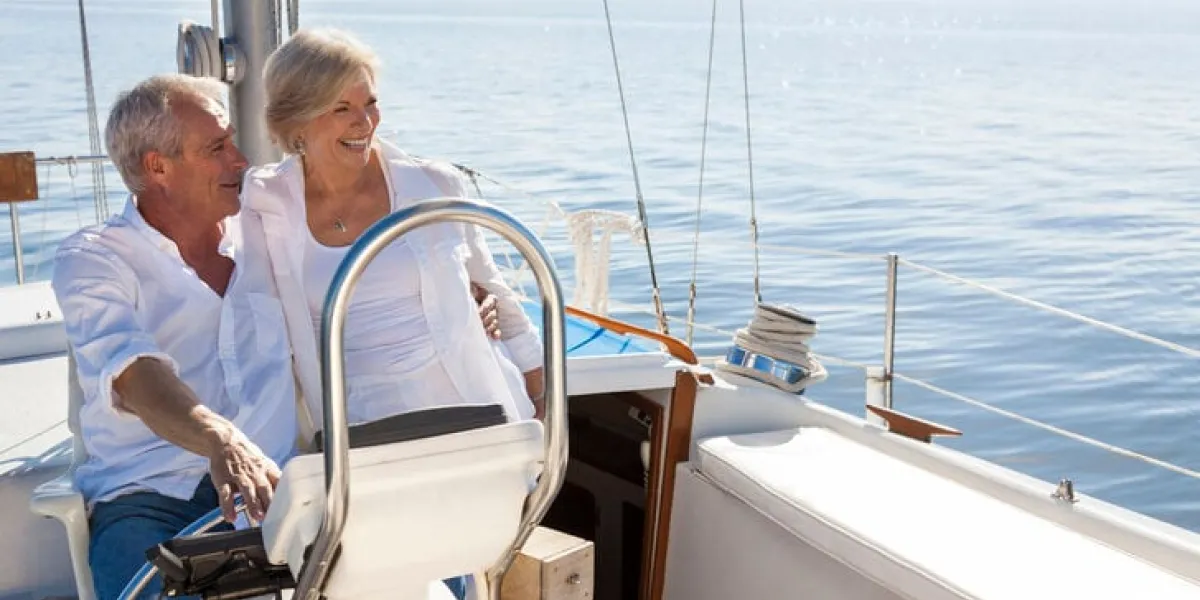 a happy senior couple sailing and sitting at the wheel of a sail boat on a calm blue sea