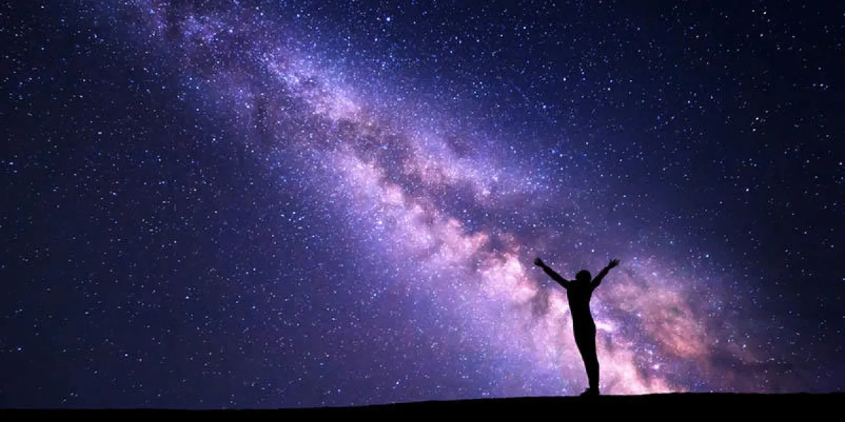 landscape with colorful purple milky way night sky with stars and silhouette of a standing sporty girl with raised-up arms on the hill beautiful universe space background