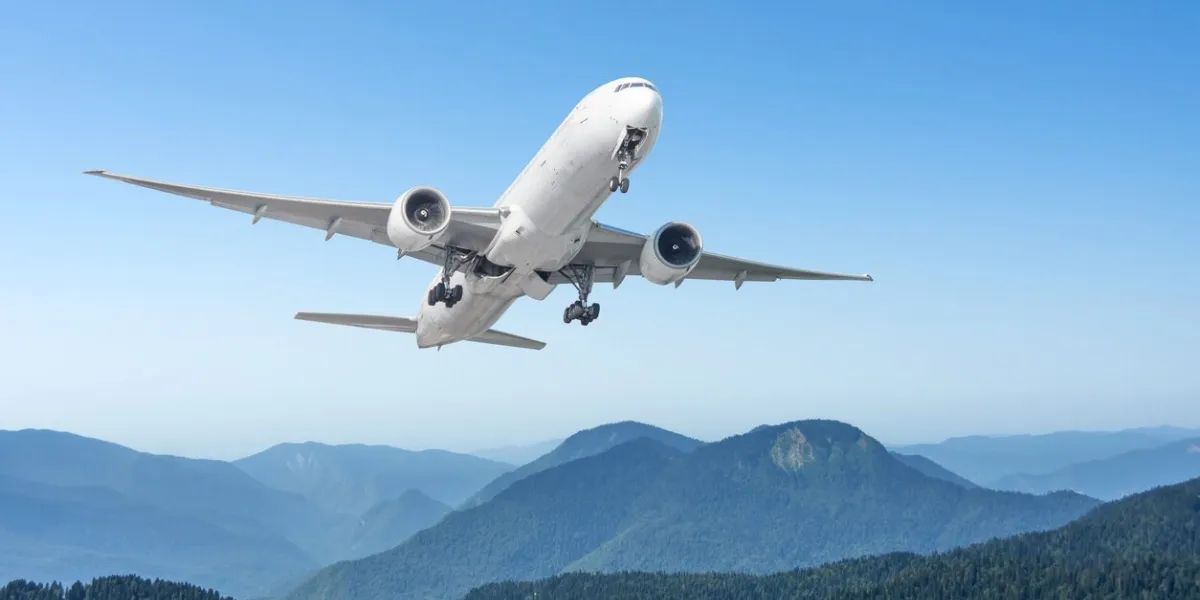 commercial passenger airliner with extended landing gear flies over mountain rocky hilly landscape on a clear sunny day