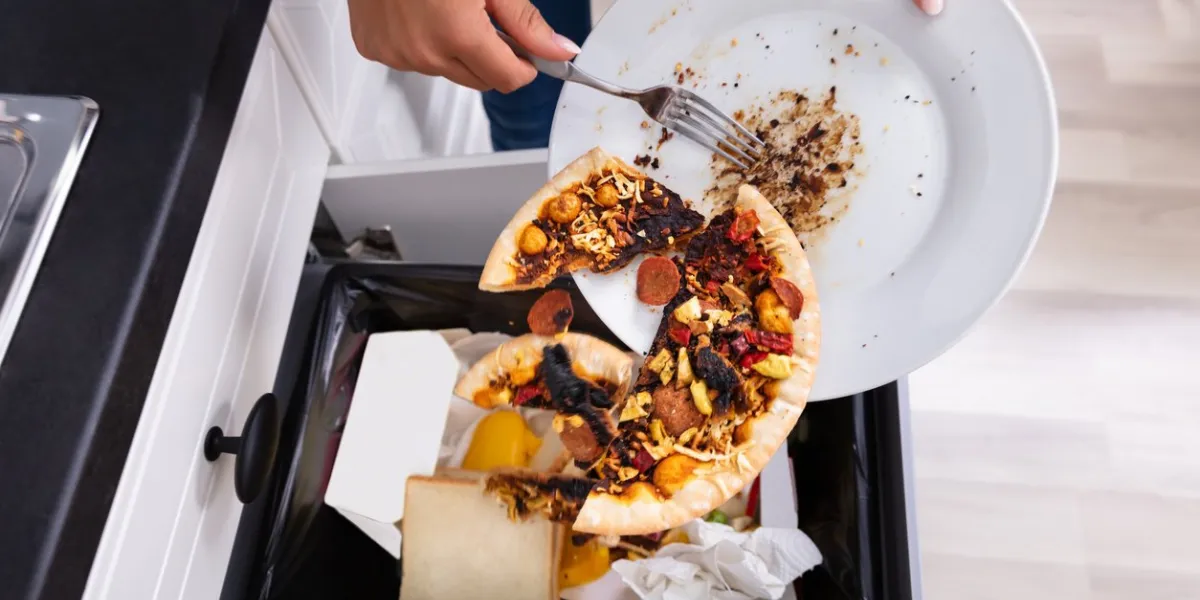 close-up of a person throwing pepperoni pizza on plate in dustbin
