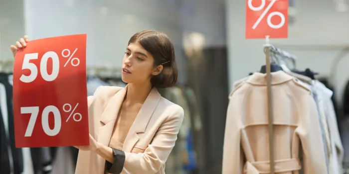 waist up portrait of beautiful woman hanging red sale signs on window display in clothes store, copy space