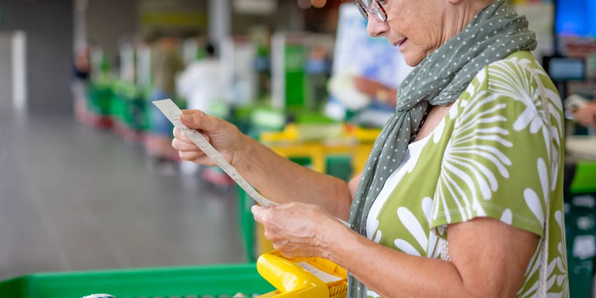 senior woman in the supermarket checks her grocery receipt looking worried about rising costs - consumerism concept, rising prices, inflation