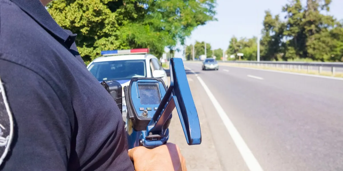police officer holding laser speed gun near police car on highway background selective focus, part of body