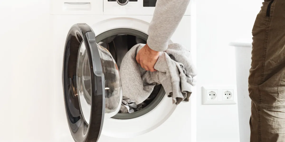 side view putting clothes in washing machine in the home laundry