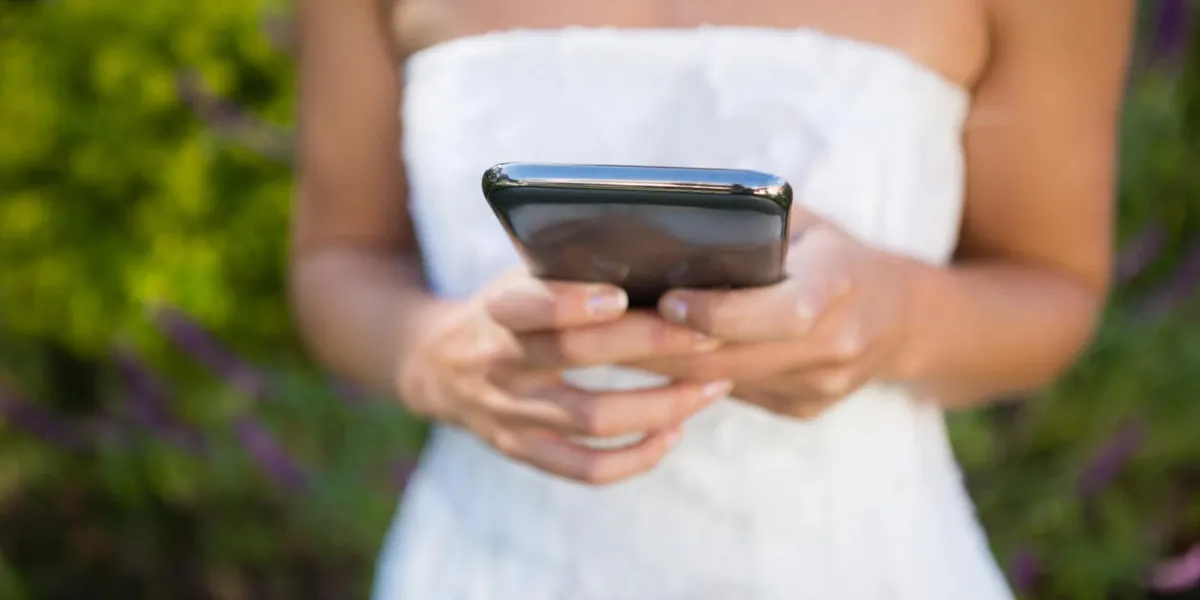 midsection on bride using mobile phone while standing against plants in yard