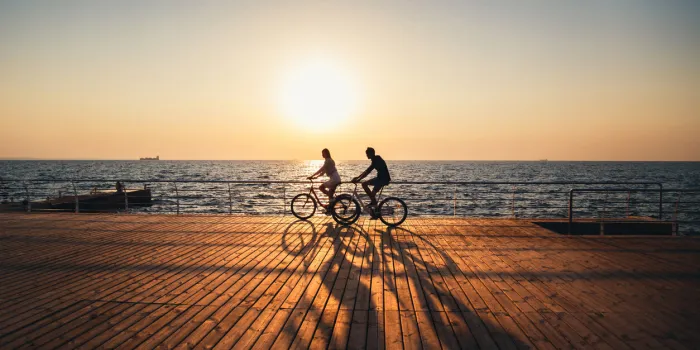 couple of young hipsters cycling together at the beach at sunrise sky at wooden deck summer time