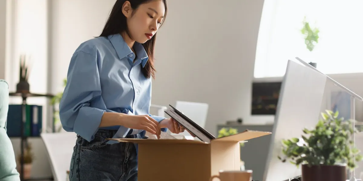 sad unemployed asian woman packing personal belongings in cardboard box standing at table desk, feeling stressed and depressed losing her job upset dismissed lady leaving office after being fired