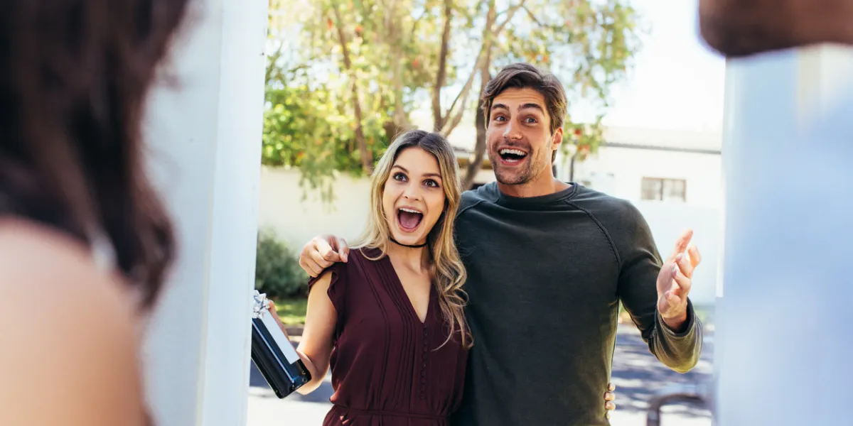 excited couple at entrance door with bottle of wine friends being welcomed by couple at the door attending friend's housewarming party