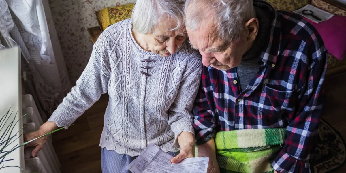 the senior woman and man holding gas bill in front of heating radiator payment for heating in winter