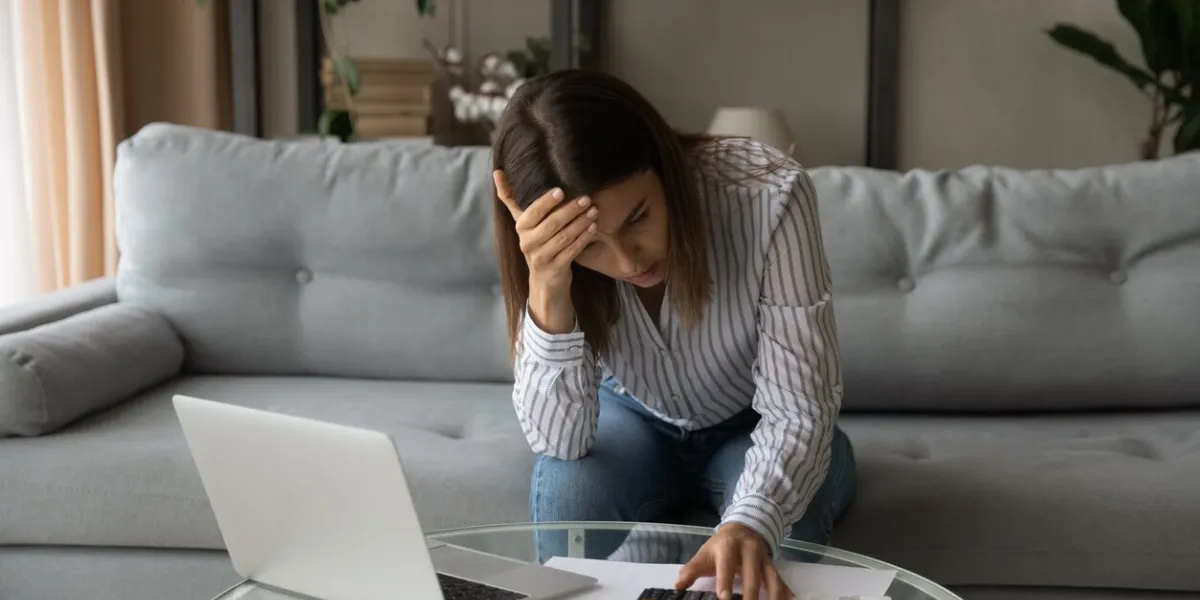 desperate young woman sit on sofa at home calculates expenses feeling stressed about bank loan payments, lack of money, financial problems, thinking of unpaid taxes, bankruptcy, overdue bills concept