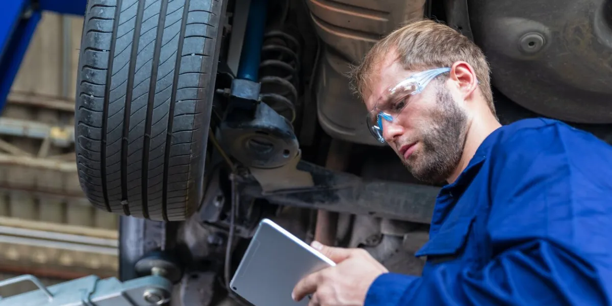 a male auto mechanic in uniform is examining a tire while working in auto service