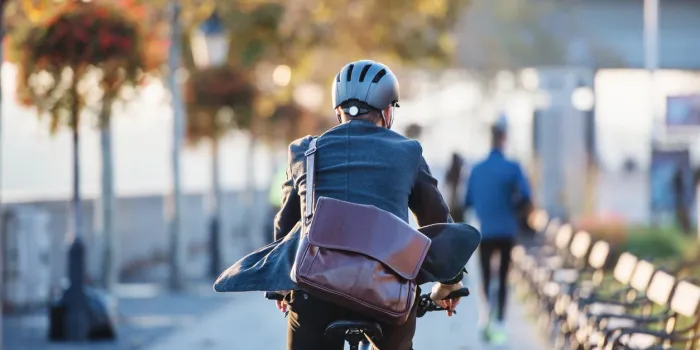 a rear view of a businessman commuter with electric bicycle traveling to work in city copy space