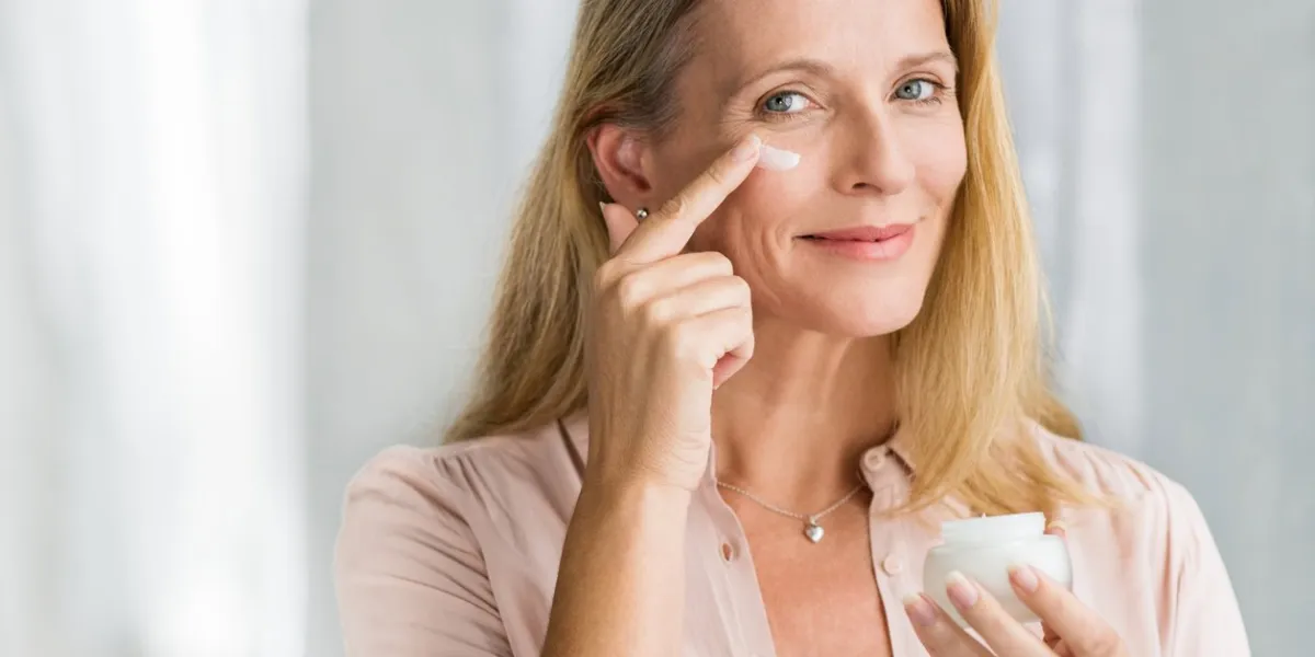 smiling senior woman applying anti-aging lotion to remove dark circles under eyes happy mature woman using cosmetic cream to hide wrinkles below eyes lady using day moisturizer to counteract the aging of the skin