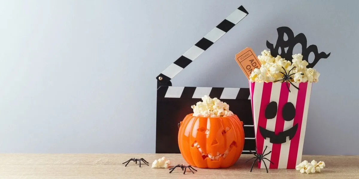 horror movie night and halloween party concept with jack o lantern pumpkin, popcorn and movie clapperboard on wooden table