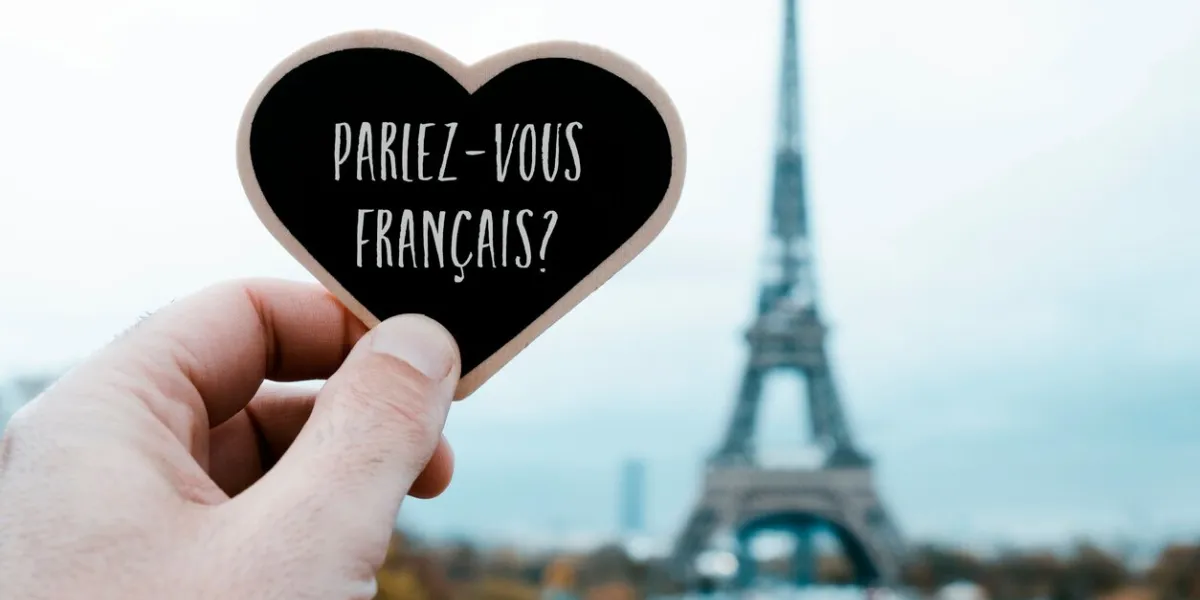 closeup of a young man holding a heart-shaped signboard with the question do you speak french written in french in it, in front of the eiffel tower in paris, france