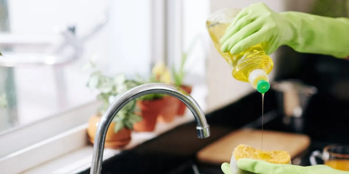 closeup image of woman in latex gloves pouring dish soap on sponge and washing dishes