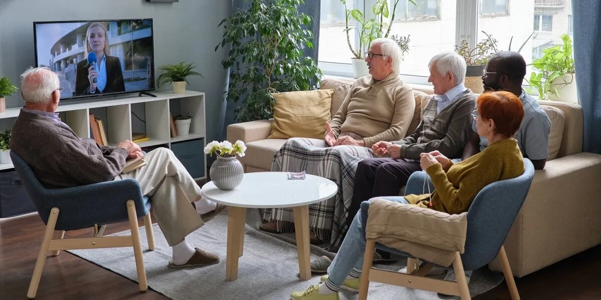 group of senior people resting on sofa in the living room and watching news on tv together