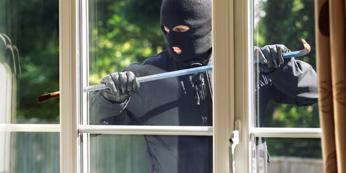 burglar breaking into a house via a window with a crowbar