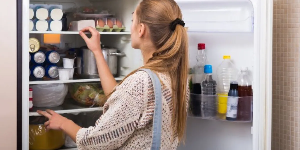 young housewife arranging products on fridge shelves