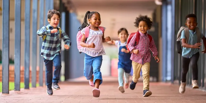 group of multi-cultural elementary school pupils running along walkway outdoors at school