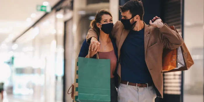 the young couple carries shopping bags and walks through the mall, wearing protective masks, life in a time of pandemic