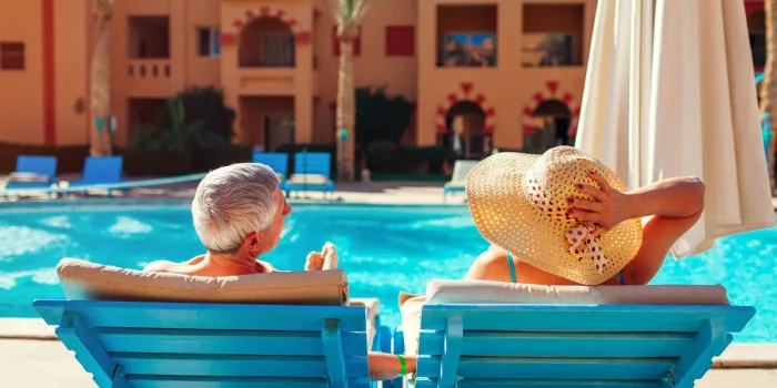 senior family couple relaxing by swimming pool lying on chaise-longues people enjoying summer vacation