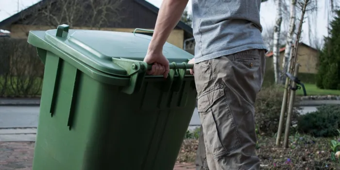 man pushing a green garbage bin