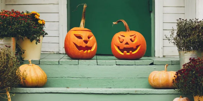 staircase autumn decor house entrance with halloween pumpkin decoration on wooden stairs, two jack o lanterns with spooky faces on porch of apartment building during all hallows eve