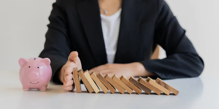 businesswoman protecting piggy bank from falling wooden blocks on the table, financial business concept