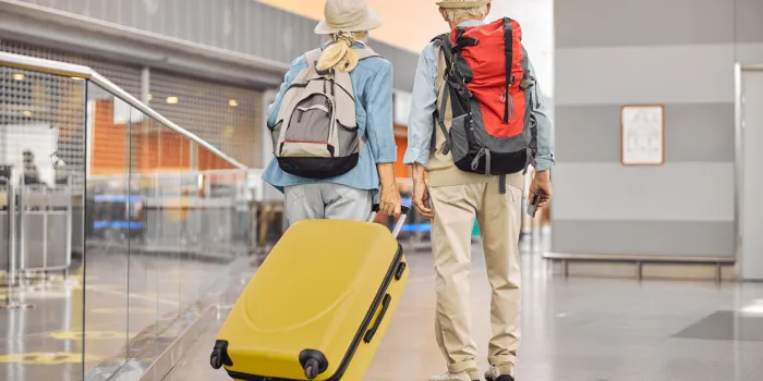 back view of a senior lady with a trolley suitcase and a man with a boarding pass