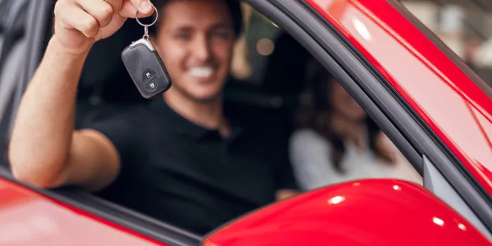 blurred smiling man showing key of just bought automobile sitting with girlfriend in car