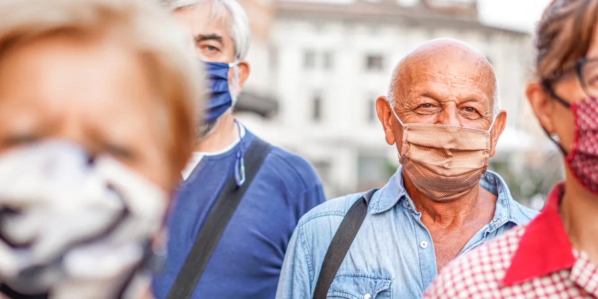 crowd of people walking down the city streets with face mask on - camera focusing an old man - new lifestyle