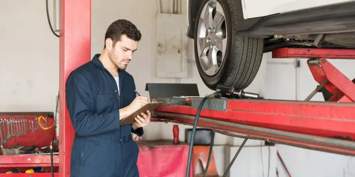 auto technician making checklist while standing by car in garage