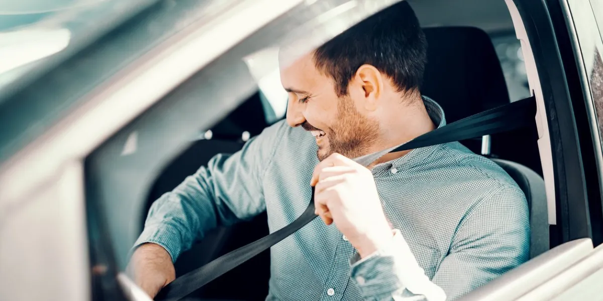 portrait of smiling caucasian man fastening seat belt and sitting in his car window opened, side view
