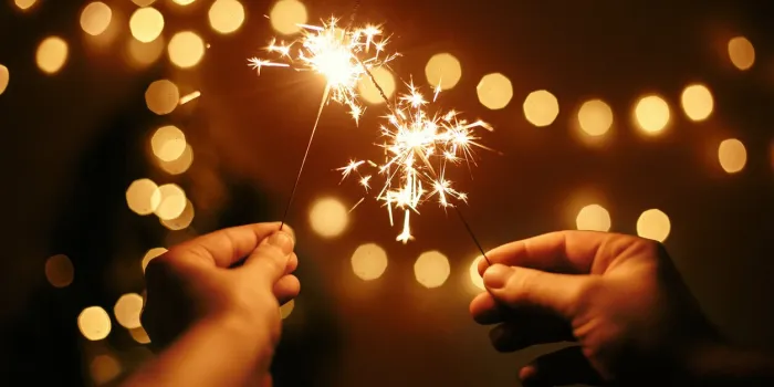 glowing sparklers in hands on background of golden christmas tree lights, couple celebrating in dark festive room happy new year space for text fireworks burning in hands happy holidays