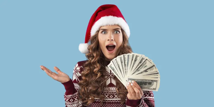 special christmas offer shocked millennial girl in winter outfit holding fan of money on blue background, panorama