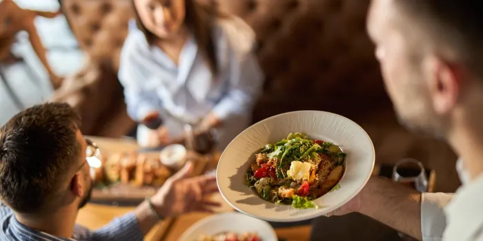 close up of unrecognizable man holding plate with food while serving group of business people during lunch time in a restaurant focus is on a plate