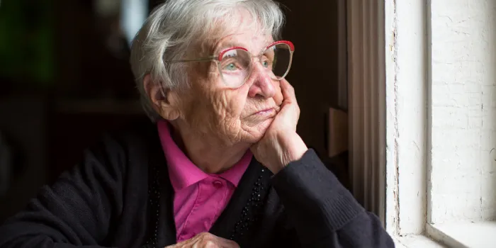 elderly woman in glasses thoughtfully looking out the window